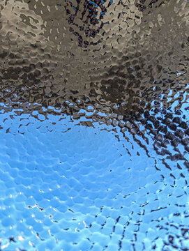 Close-up of Silver-Plated Hammered Metal Bowl Reflecting Clear Blue Sky.