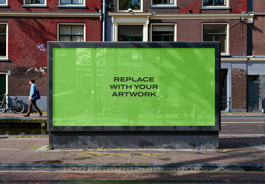 Large vertical billboard mockup with placeholder screen displaying replace your artwork text, situated on a city sidewalk in front of red brick building, urban advertising display