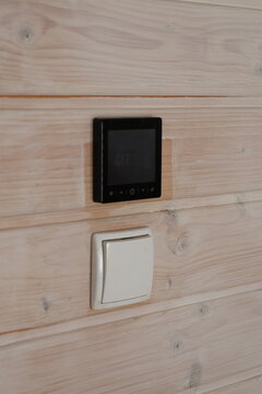 Smart digital thermostat and light switch on wooden wall. Modern digital smart thermostat and light switch on wooden wall for indoor temperature control.