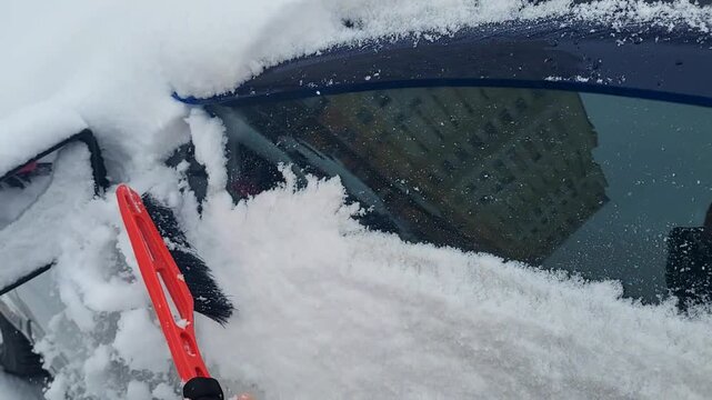 Cleaning snow from a car windshield with a brush during winter, seasonal maintenance, morning routine, cold weather activity. Winter.