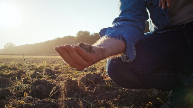 Man hand takes and pours out handful of dry soil in bare field