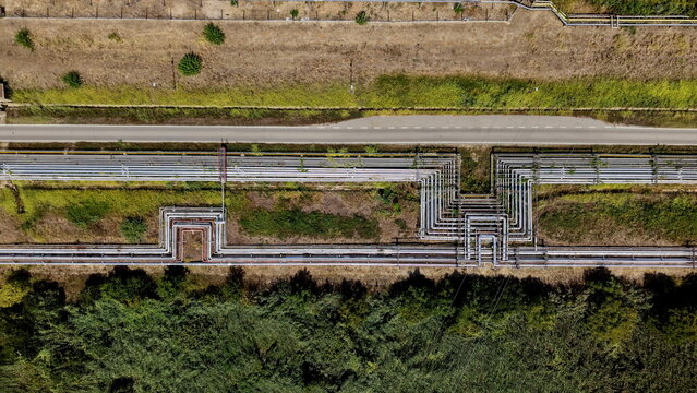Aerial view of petrochemical industry pipelines running parallel to a road through green fields in Pancevo, Serbia.
