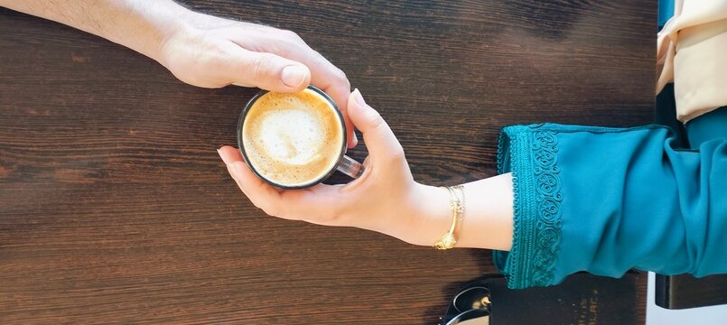 Couple hands sharing latte coffee, woman wearing Moroccan caftan