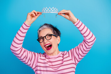 Joyful older woman holding a sparkly tiara above her head celebrating playful confidence and self expression © deagreez