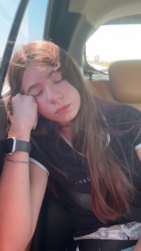 Tired teenage girl sleeping peacefully in the back seat of a moving car during a sunny day, showcasing a moment of tranquility and relaxation on a family road trip