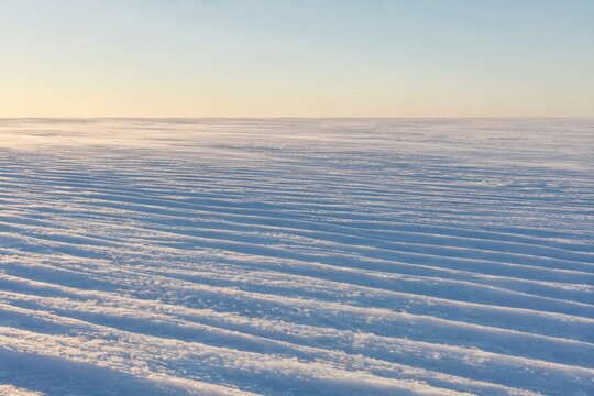 Wind carved ripples across an empty frozen snowfield at dawn