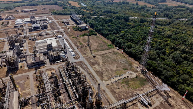 Aerial view of the petrochemical industry facility with complex piping, storage tanks, and a flare stack emitting a flame, situated in a rural landscape near Pancevo, Serbia.