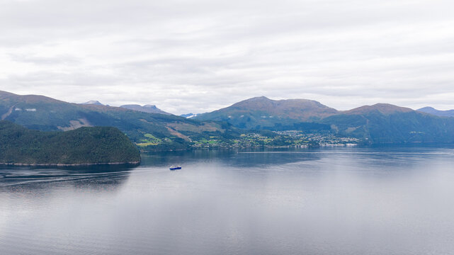 Aerial view of a wellboat navigating the calm waters of a fjord surrounded by rolling mountains and green hills in Stranda, More og Romsdal, Norway.