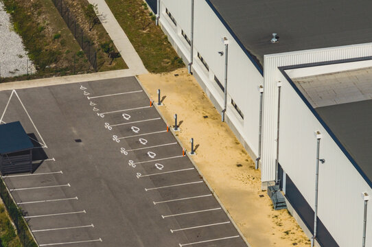 Aerial view of electric vehicle charging stations beside a modern industrial building and empty parking spaces in Le Pouzin, Auvergne-Rhone-Alpes, France.