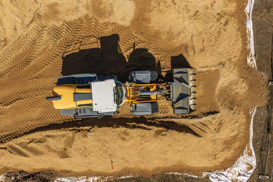 Aerial view of a yellow wheel loader leveling sand at the Lincolnsiedlung construction site in Darmstadt, Hessen, Germany.