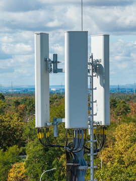 Aerial view of cellular antenna array at Lincolnsiedlung with cables and metal structures against a backdrop of green trees and a cloudy sky in Darmstadt, Hessen, Germany.