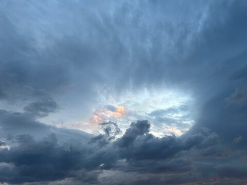 Powerful stormy sky with massive blue-gray clouds surrounding a glowing opening filled with golden-pink sunset light.