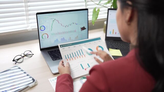 Businesswoman analyzing financial graphs and stock market charts on laptop and paper document