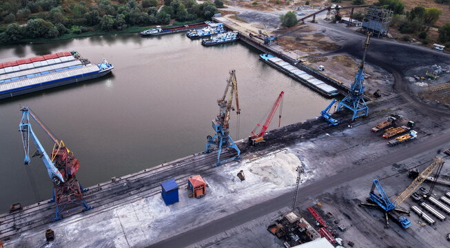 Aerial view of the Danube Port in Pancevo with industrial cargo cranes, docked barges, and loading infrastructure along the riverbank in Pancevo, Serbia.