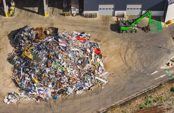 Aerial view of a scrap metal recycling yard with a large pile of mixed industrial waste and a material handler beside a waste processing facility in Le Pouzin, Auvergne-Rhone-Alpes, France.
