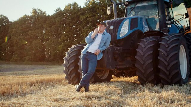 Farmer in shirt chews straw while leans on combine harvester