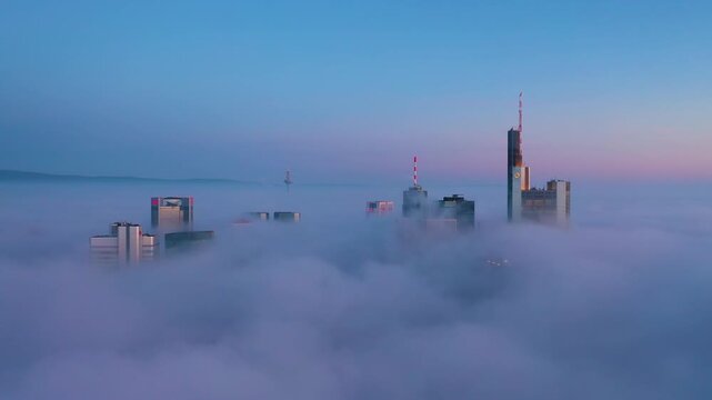 Aerial view of the Frankfurt skyline emerging from a dense layer of morning fog, with skyscrapers piercing through the clouds in Frankfurt am Main, Hessen, Germany.