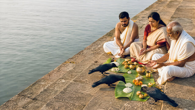 An Indian family performs Pitru Paksha ancestral rituals while black crows feed on sacred rice offerings along the riverbank