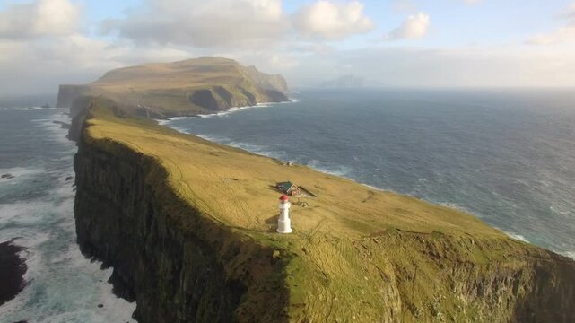 Aerial view of Kallur Lighthouse perched on the edge of a dramatic grassy cliff overlooking the North Atlantic Ocean in the Faroe Islands.