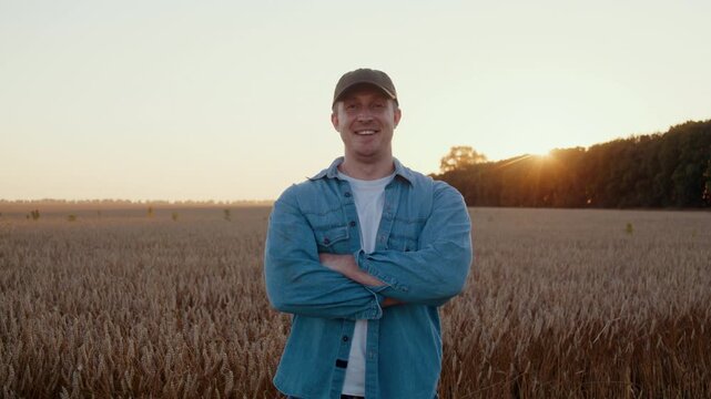 Confident farmer stands with crossed arms in ripe wheat field