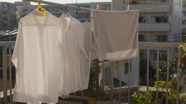White shirts and towel hanging to dry on balcony clothesline outdoors