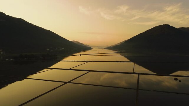 Aerial view of salt pans reflecting the golden sunset light between hills in Croatia.