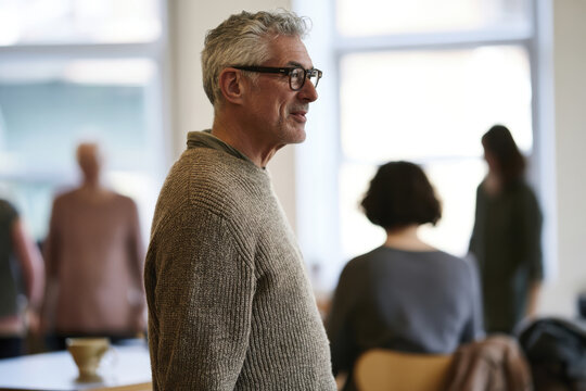 A confident middle-aged man stands in a social setting, embodying the essence of self-assurance and engagement amid a gathering of thoughtful individuals.