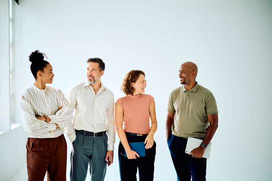 Diverse team of professionals standing together, discussing and smiling, showing successful collaboration and teamwork in a modern office