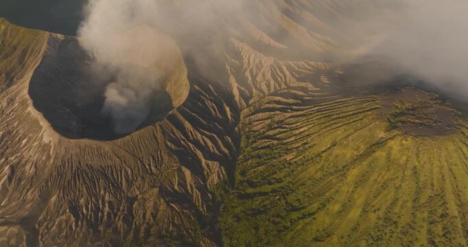 Aerial view of Mount Bromo and Tengger Caldera with volcanic smoke rising from the crater and rugged green slopes in Indonesia.