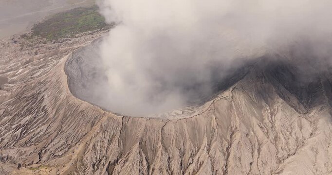 Aerial view of the active volcanic crater of Mount Bromo and the surrounding Tengger Caldera with thick smoke rising from the vent and rugged volcanic terrain in Indonesia.