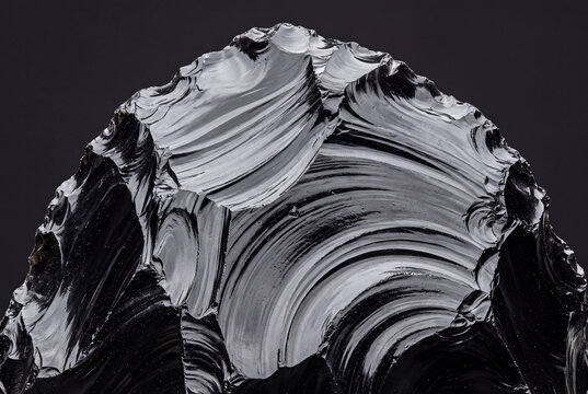 Broken obsidian macro with glassy conchoidal fracture on solid charcoal background