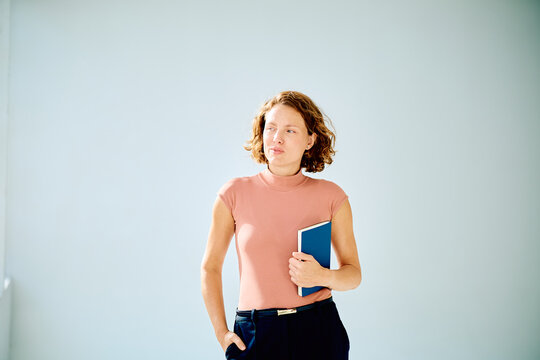 Mid aged woman contemplating ideas, holding a notebook, wearing casual professional attire in a studio portrait with copy space