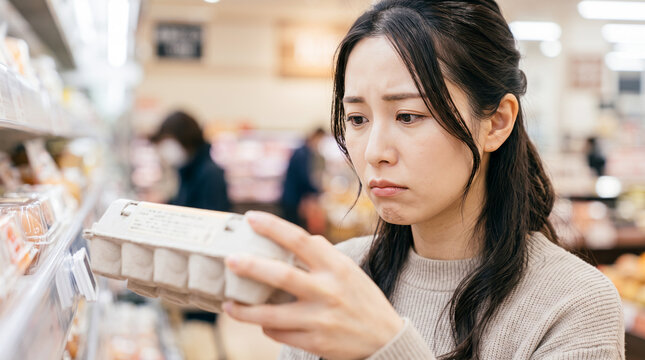 スーパーで卵の価格や品質に悩む困り顔の女性