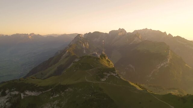 Aerial view of the Alpstein mountain range at sunset, featuring the Hoher Kasten summit with its communications tower, rugged peaks, and green slopes in Appenzell, Appenzell Innerrhoden, Switzerland.