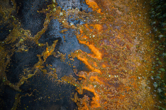 Aerial view of the vibrant orange and dark brown peatland landscape with winding water channels and patches of coniferous forest in Kittila, Lapland, Finland.