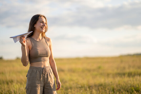 Young woman holding paper airplane in sunny field looking away