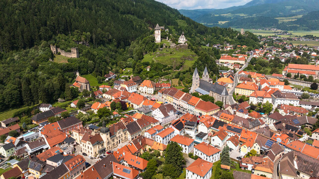 Summer drone footage showing medieval Friesach, old fortified walls, rooftops, towers, hills, serene atmosphere, warm daylight, gentle cinematic motion