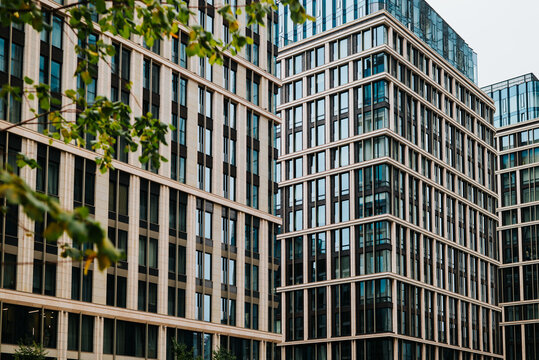 several modern buildings featuring glass facades and geometric designs in an urban area. The buildings have a mix of dark and light materials, reflecting the surrounding environment