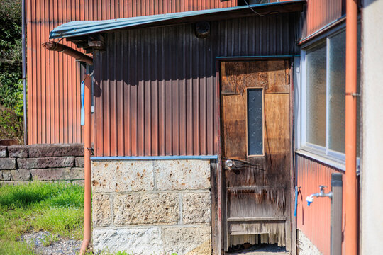 Retro Old Building with Rust-Red Corrugated Metal Wall, Stone Foundation, and Wooden Door