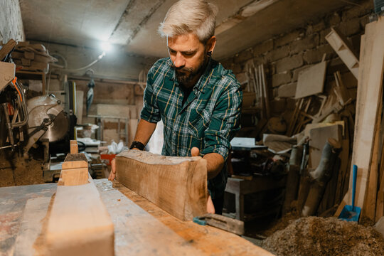 Carpenter shaping a wooden beam in a cluttered rustic workshop concentrating on a woodworking project
