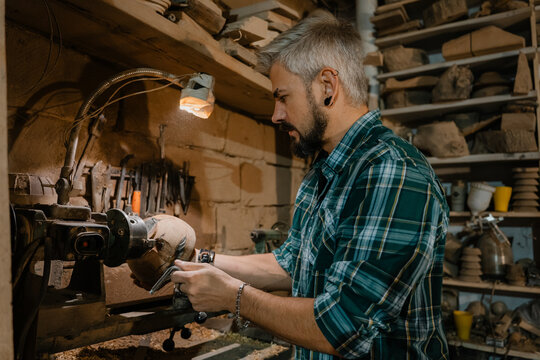 Woodworker shaping a wooden bowl on a lathe in a rustic workshop, focused male craftsman at work