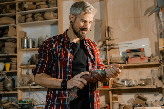 Middle-aged craftsman using electric drill in cluttered woodworking workshop, focused on detail