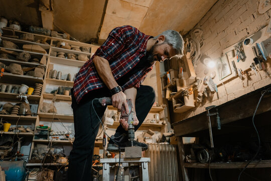 Skilled woodworker drilling into a wooden block in a cluttered workshop using a power drill