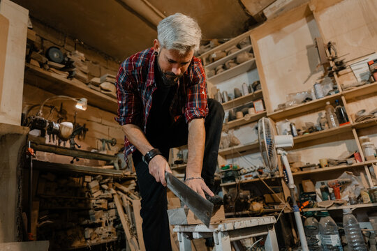 Carpenter sawing a wooden plank in a cluttered woodworking workshop concentrating on his craft