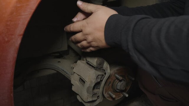 Professional auto mechanic unscrewing a bolt on a car brake caliper with a wrench during a maintenance service in a repair shop, ensuring vehicle safety and performing necessary repairs