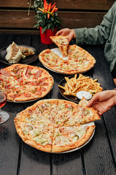 Group of diners share assorted pizzas, French fries, grilled wrap and drinks around a dark outdoor restaurant table, creating a casual social dining scene