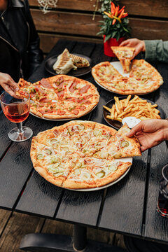 Group of diners share assorted pizzas, French fries, grilled wrap and drinks around a dark outdoor restaurant table, creating a casual social dining scene