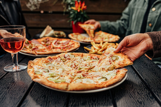 Group of diners share assorted pizzas, French fries, grilled wrap and drinks around a dark outdoor restaurant table, creating a casual social dining scene