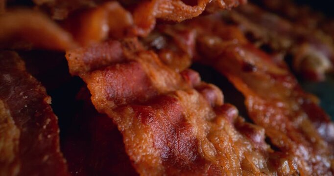 Crispy bacon sizzling on a hot griddle as the camera glides extremely close across its surface, revealing bubbling fat, rich texture and an irresistible freshly cooked, cinematic food moment.