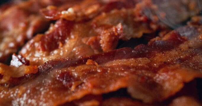 Crispy bacon sizzling on a hot griddle as the camera glides extremely close across its surface, revealing bubbling fat, rich texture and an irresistible freshly cooked, cinematic food moment.